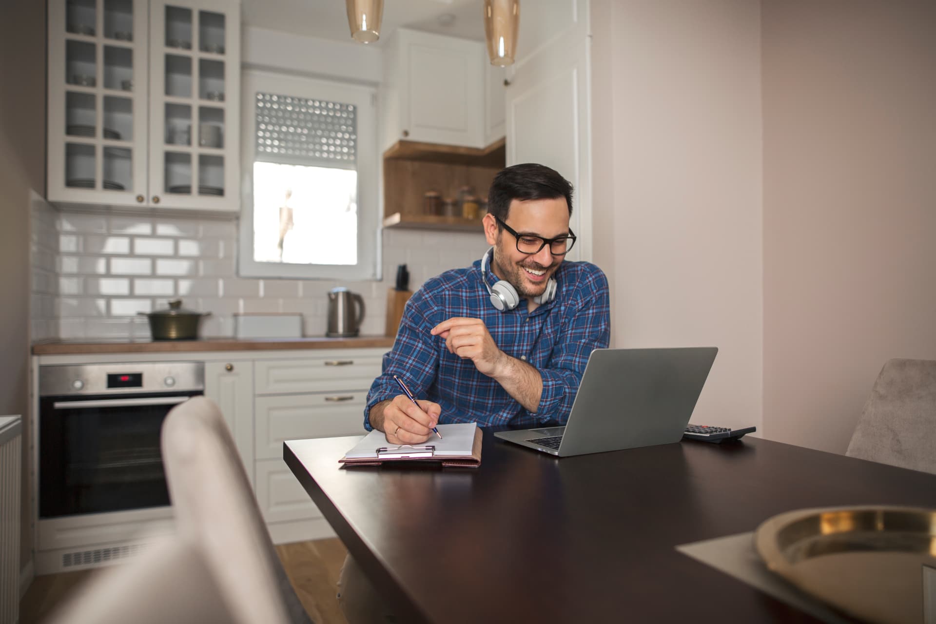 A clinician smiling during a video visit while taking notes at his kitchen table